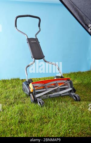 Mowing the lawn by hand. Symbolic photo, spindle mower on lawn against light blue, sky Stock Photo