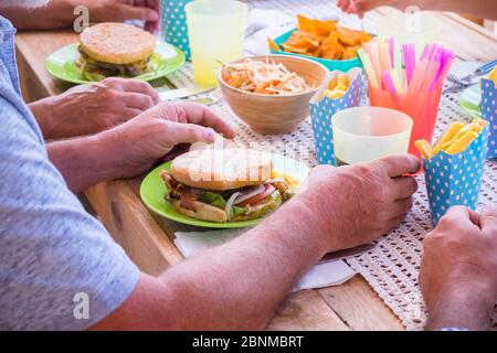 A group of older people enjoy a fast food lunch together with handmade hamburgers and French fries on a wooden table, unhealthy lifestyle Stock Photo