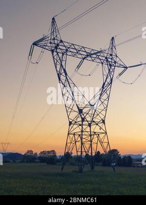 High voltage transmission power line tower with orange sunset background. Electricity, power distribution and technology concepts Stock Photo