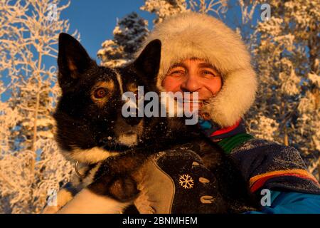 Nils-Torbjörn Nutti, owner and operator at Nutti Sami Siida, with domestic husky dog, during snowmobile trip into the wilderness, Jukkasjarvi, Lapland Stock Photo