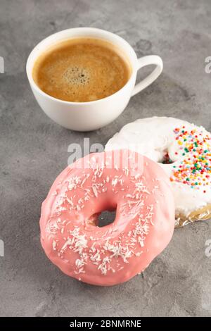White cup of coffee and two donuts in white and pink icing on grey background Stock Photo
