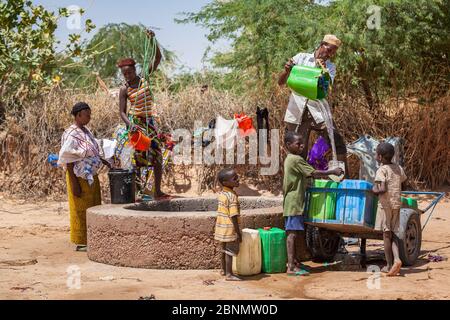 people filing plastic containers with water at public well in desert oasis Stock Photo