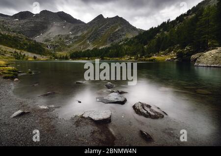 Dramatic sky and water flowing in dark day over the Lac d’Arpy, beautiful alpine mountain lake near Morgex (Aosta Valley, Italy) and the Mont Blanc Stock Photo