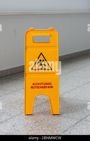 Caution wet floor or cleaning in progress. A yellow sign warns of danger. Stock Photo