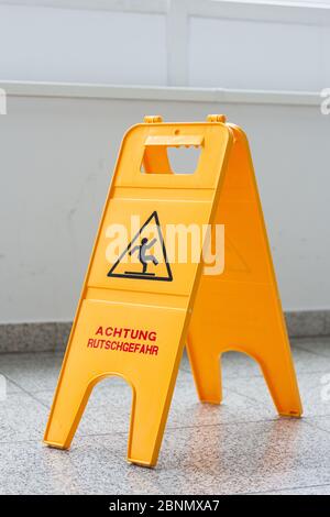 Caution wet floor or cleaning in progress. A yellow sign warns of danger. Stock Photo