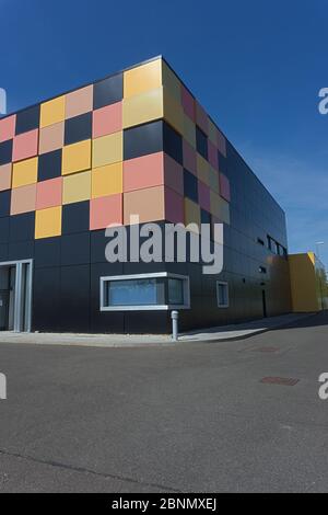 Matt black cubic building with yellow and red tiles in one corner as graphic design behind metal security railings intense blue sky data centre Stock Photo