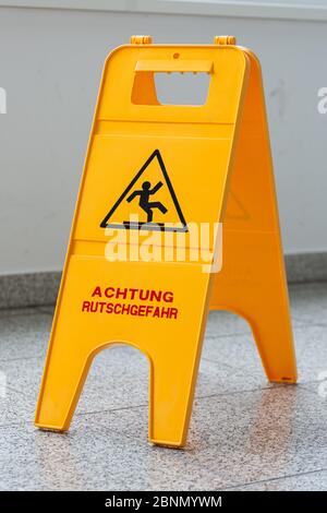 Caution wet floor or cleaning in progress. A yellow sign warns of danger. Stock Photo