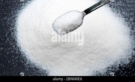 Sugar falling from spoon on black background. Stock Photo