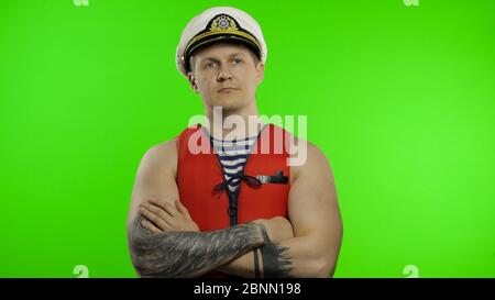 Young muscular sailor man works as lifeguard at beach observe the territory. Seaman guy life saver in sailor's vest, lifejacket, captain nautical hat. Isolated on chroma key background. Green screen Stock Photo