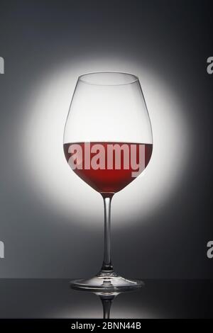 Glass with red wine on a gray background with backlight and reflection. Stock Photo