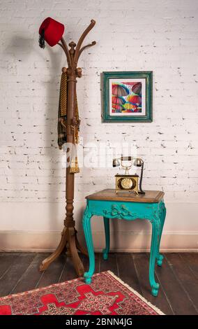 Green Wooden Vintage Side Table With Golden Antique Telephone Set And Coat Hanger Stand With Red Fez And Scarf On Room With White Bricks Wall Hanged Painting And Wooden Parquet Floor Stock