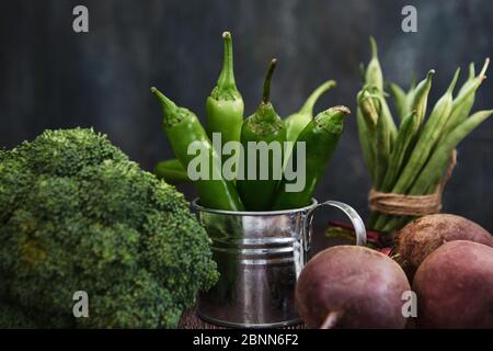 Green hot pepper in an enameled watering can, broccoli and beets on a dark wooden background. Stock Photo