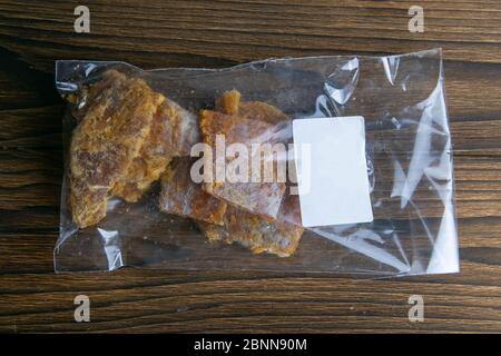 Dried cod with pepper in a transparent package with a white label appetizer to beer on wooden background. Snack Fish to beer. Close up Stock Photo