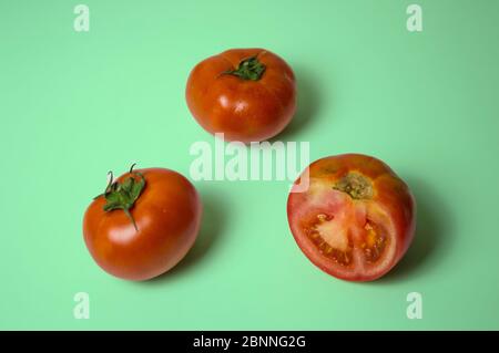 Two whole tomatoes and one match on green background Stock Photo