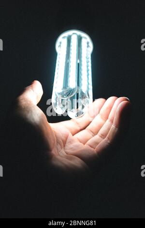 Led light bulb on illuminating a human hand on dark background Stock Photo
