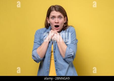 Shocked amazed young woman with hands on chest standing and shouting over yellow background Stock Photo