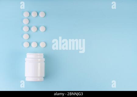 Vitamin E pills dropped from bottle on blue. Letter E inscription from tablets. Vitamin E concept. Immunity protection concept, antiviral prevention. Stock Photo