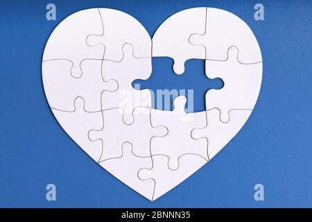 Love, charity, donation, helping concept. Missing piece of jigsaw puzzle in heart shape on blue. Looking for love partner. Uncompleted puzzle. Relatio Stock Photo