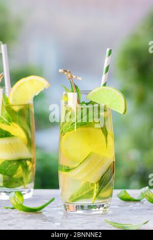 Two glasses of lemonade or mojito cocktail with lemon, cucumber and mint, cold refreshing drink or beverage with ice and paper straw, outdoor. Summer Stock Photo