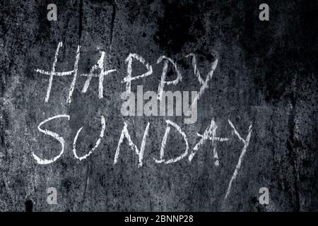 Happy Sunday wrote on the rough wall with yellow-colored chalk, close up horizontal shot. Stock Photo