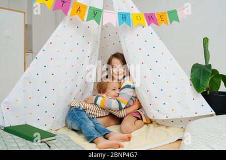 Kids hugging inside a hut at home, sitting on a blanket Stock Photo