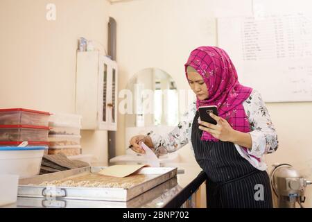 woman in her workshop baking some cake and checking her product using mobile phone Stock Photo