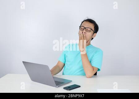 Young Asian Man is Lazy and tired with sleep when working in the front of Laptop. Indonesian man wearing blue shirt. Stock Photo