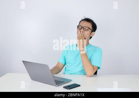 Young Asian Man is Lazy and tired with sleep when working in the front of Laptop. Indonesian man wearing blue shirt. Stock Photo