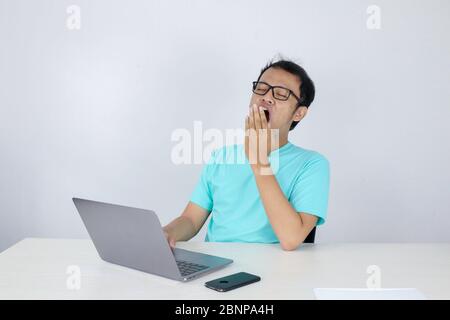 Young Asian Man is Lazy and tired with sleep when working in the front of Laptop. Indonesian man wearing blue shirt. Stock Photo