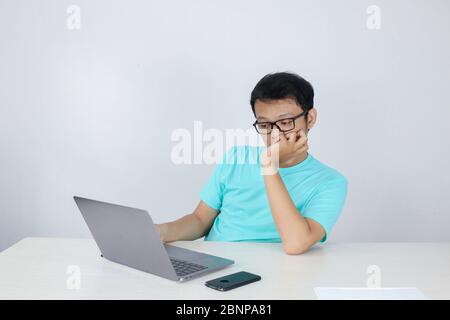 Young Asian Man is Lazy and tired with sleep when working in the front of Laptop. Indonesian man wearing blue shirt. Stock Photo