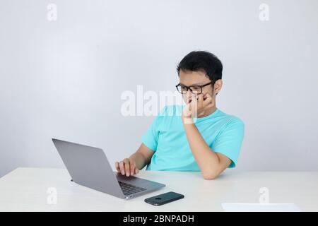 Young Asian Man is Lazy and tired with sleep when working in the front of Laptop. Indonesian man wearing blue shirt. Stock Photo
