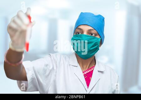 Medical worker, nurse wearing surgical mask holding test tube with blood sample of the Coronavirus patient for the testing purpose, Covid=19 Pandemic. Stock Photo