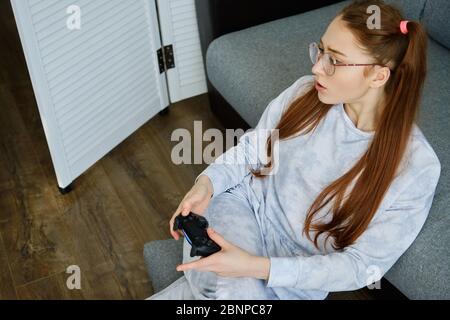 Redhead girl in pajamas sits on the floor with a game joystick, the view from above. Stock Photo