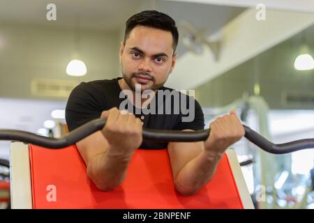Young bearded Indian man lifting weights at the gym Stock Photo