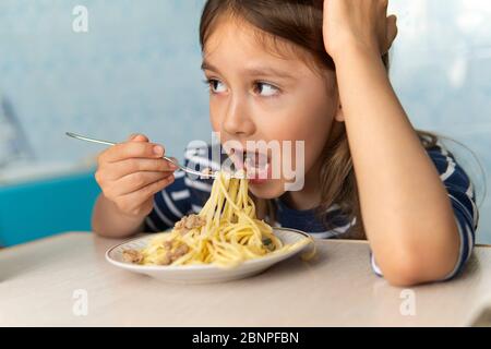 Kids eat pasta. Healthy lunch for children. Toddler kid eating spaghetti Bolognese in a blue kitchen at home. Preschooler child try noodles for dinner Stock Photo