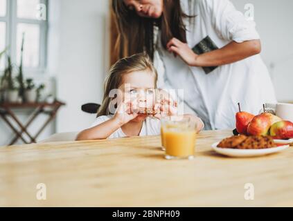 Young mother brush her little daughter's hair during breakfast at table at home, morning routine Stock Photo