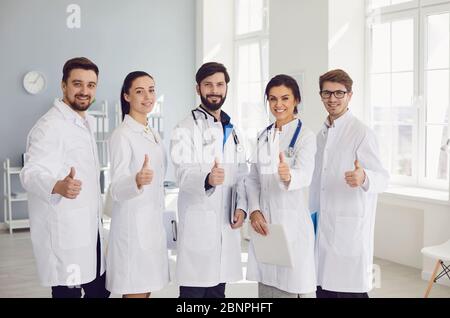 Group of practicing doctors with stethoscope thumbs up are smiling while standing in the clinic office. Positive group of doctors at the hospital. Stock Photo
