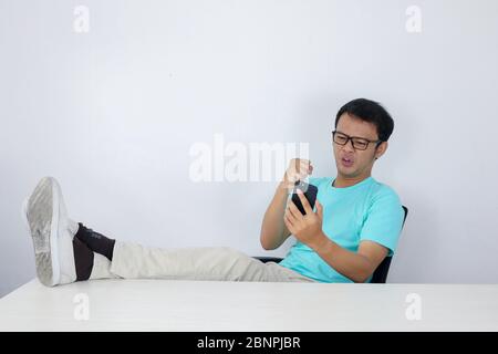 Angry Asian young man get mad when call on the smartphone. Indonesian man wearing blue shirt. Stock Photo