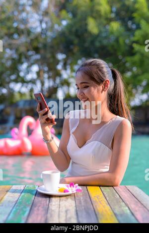 Happy young beautiful Asian woman using phone outdoors Stock Photo