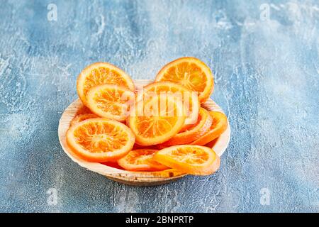 Slices of dried oranges or tangerines in a wooden plate on a blue background. Vegetarianism and healthy eating. Copy space. Stock Photo