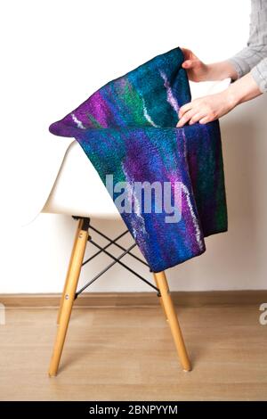 Bright blue-violet silk wool scarf made hand-made by an unidentified woman designer lies on light chair on white background. Concept of unique natural Stock Photo
