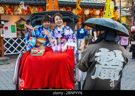 Japan, Honshu, Tokyo, Asakusa, Two Young Women Dressed in Kimono Riding in Rickshaw Stock Photo