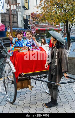 Japan, Honshu, Tokyo, Asakusa, Two Young Women Dressed in Kimono Riding in Rickshaw Stock Photo