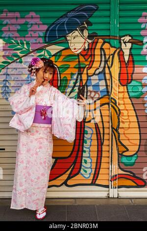 Japan, Honshu, Tokyo, Asakusa, Woman in Kimono Taking Selfie Photos in front of Colourful Store Shutter Painting Stock Photo