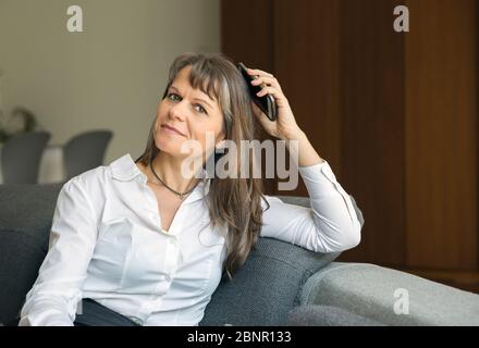 middle aged woman in formalware in her city apartment, holding a phone Stock Photo