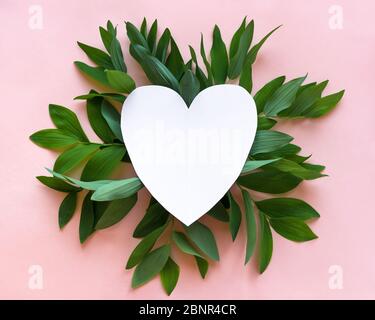 Creative layout of green leaves, wild plants on pink and white empty heart shape frame, copy space. Summer, spring or ecology design, love concept. Stock Photo