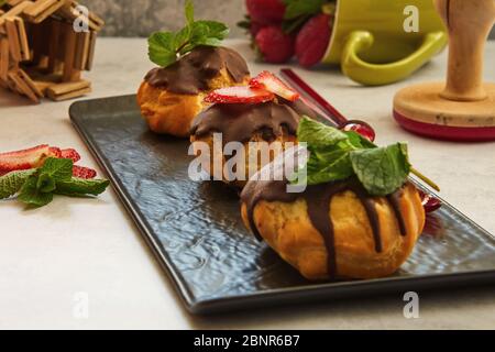 Stack eclair of profiteroles with dark melted chocolate on a black dish. Sprinkle with powdered sugar Stock Photo