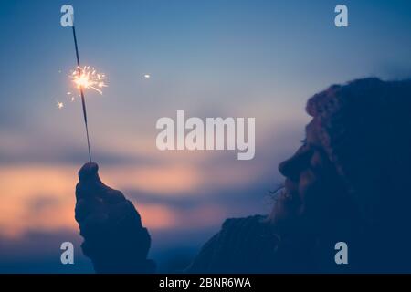 close up of woman looking at sparkler the night of the new year at the evening alone and lonely - lady playing with sparkler outdoors Stock Photo