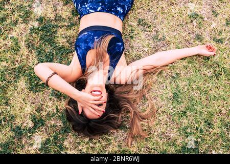 Young happy and cheerful caucasian woman relaxing and laughing after a sport exercise class or session - beautiful healthy girl lay down on the grass feeling happiness - long beauty hair Stock Photo