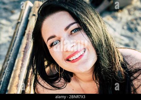 Beautiful caucasian young woman portrait smile at the camera - cheerful happy people with blue eyes and long black hair in outdoor leisure activity alone